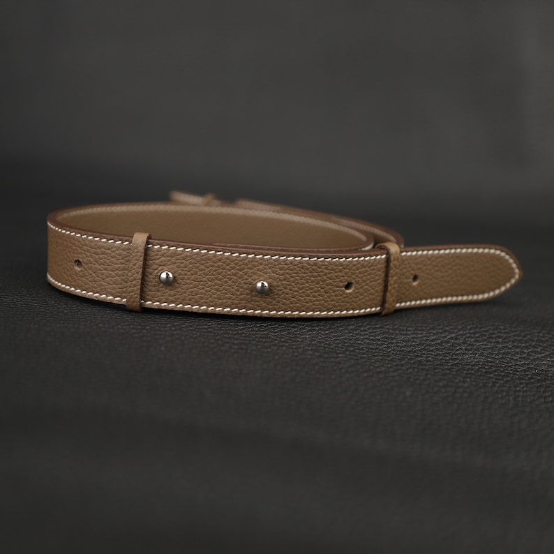 Peut inclure: Une ceinture en cuir marron avec des coutures blanches et des rivets argent&eacute;s.
