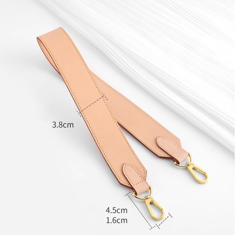 May include: A light pink leather strap with gold metal clasps. The strap is 4.5 inches long and 1.6 inches wide. The strap is 3.8 inches wide at the widest point.