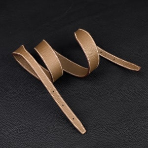 May include: A brown leather strap with white stitching. The strap is folded in a loop shape.