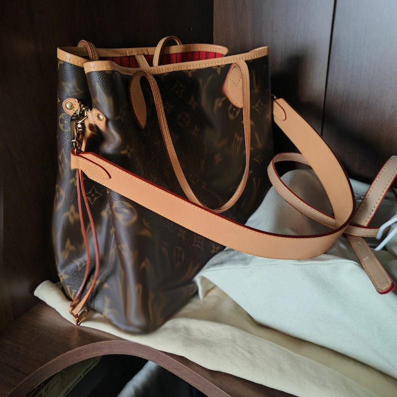 May include: A brown and tan leather tote bag with a brown and tan monogram pattern. The bag has a long strap and a top handle.
