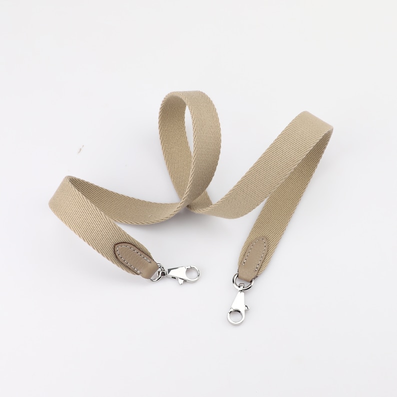May include: A beige canvas shoulder strap with leather accents and silver clasps.