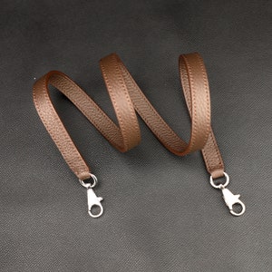 May include: A brown leather strap with silver clasps. The strap is coiled and ready to be attached to a bag or other item.
