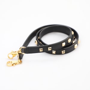 May include: Black leather strap with gold pyramid-shaped studs. The strap has two gold clasps.
