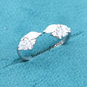 Op de afbeelding: Open zilveren ring met clusters van heldere, marquise-geslepen stenen aan elk uiteinde. De ring heeft kleinere, ronde stenen tussen de marquise-geslepen stenen. De tekst "TheMissingPieceIN" is zichtbaar.