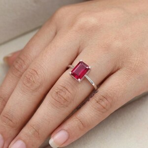 May include: A silver ring with a rectangular, deep red gemstone. The ring is set on a slender band, highlighting the vibrant colour of the stone. The MissingPieceIND is visible on the side of the ring.