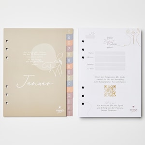 May include: A beige planner with a monthly calendar and numbered tabs. The left page has the month "Januar" written in cursive. The right page has a section for personal information and a QR code.