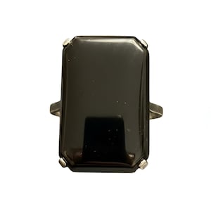 May include: A rectangular black ring with a silver band. The ring features a large, glossy, black stone with a rectangular shape and beveled edges. The silver band has a simple, elegant design.