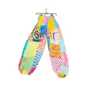 May include: Patchwork pants in a variety of colors and patterns, including floral, striped, and geometric designs. The pants are hanging on a hanger against a white background. The pants have a loose, comfortable fit with elastic at the ankles.