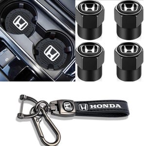 May include: A set of black Honda automotive accessories including two circular cup holder inserts with white logos, four hexagonal tyre valve stem caps with black and white logos, and a black leather keychain with a metal clip and Honda logo.