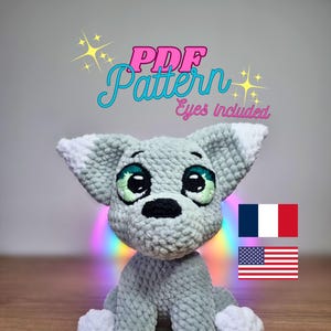 May include: A crocheted gray and white puppy amigurumi toy with blue eyes. The toy is sitting on a wooden surface. The text "PDF Pattern Eyes included" is written in pink and white letters above the toy. The flags of France and the United States are shown in the upper right corner of the image.