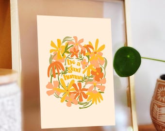 May include: A framed print with a light peach background featuring a circle of orange, yellow, and green flowers with the text "Be a good human" in the center.