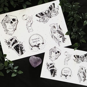 May include: Two sheets of paper with black and white illustrations of skulls, moths, hands, and a coffin. The text on the sheets reads "Fall into your eyes like a grave", "You know you hypnotize me", "I'm a messy piece, you're a texture of my", "Perfectly misaligned", "The night belongs to you", "What is coming", "I'm a messy piece, you're a texture of my", "Perfectly misaligned", "You know you hypnotize me", "The night belongs to you", "What is coming".