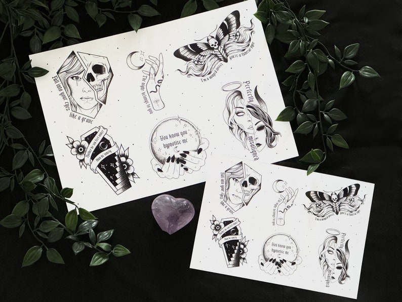 May include: Two sheets of paper with black and white illustrations of skulls, moths, hands, and a coffin. The text on the sheets reads "Fall into your eyes like a grave", "You know you hypnotize me", "I'm a messy piece, you're a texture of my", "Perfectly misaligned", "The night belongs to you", "What is coming", "I'm a messy piece, you're a texture of my", "Perfectly misaligned", "You know you hypnotize me", "The night belongs to you", "What is coming".