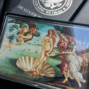 May include: A rectangular silver bar case with the text "IN SILVER" and a silver emblem that reads "AMERICAN SILVER STACKERS" with an eagle. The case contains a print of Botticelli's "The Birth of Venus."