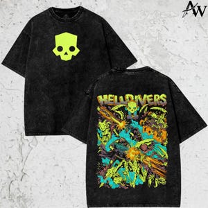 May include: Black acid wash t-shirt featuring a neon green skull graphic on the front and a colorful illustration with the text "HELLDIVERS" on the back. The shirt has short sleeves and a crew neck.