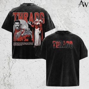 May include: Two black graphic t-shirts. One features the word "THRAGG" in red and black block letters. The other shirt has the same text, plus a graphic of a man in a red and white costume with text below.