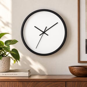 May include: A round wall clock with a thin black frame, a plain white face, and three black hands. The clock features a simple design with no numbers or markings on the dial, providing a clean and functional appearance for timekeeping.