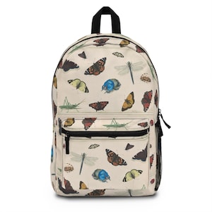 May include: Cream-coloured backpack with a repeating pattern of colourful butterflies, dragonflies, and beetles. The backpack has a black top handle, a front zipped pocket, and a side mesh pocket. The design is reminiscent of vintage botanical illustrations.