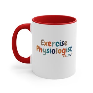 Könnte beinhalten: Weiße Keramik-Kaffeetasse mit rotem Rand und Henkel. Die Tasse trägt den Text "Exercise Physiologist est. 2024" in bunten, verspielten Buchstaben.