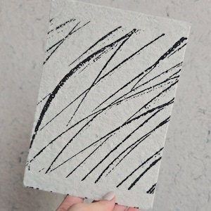 K&ouml;nnte beinhalten: Ein rechteckiges, cremefarbenes Notizbuch mit strukturierter Oberfl&auml;che. Auf dem Cover sind kr&auml;ftige, schwarze diagonale Linien aufgedruckt. Der Text "Screen printing @vickyhuangprints" ist unten rechts aufgedruckt.