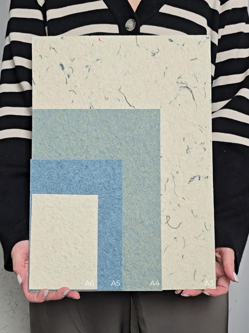 K&ouml;nnte beinhalten: Eine Sammlung strukturierter Papierb&ouml;gen in verschiedenen Gr&ouml;&szlig;en, darunter A3, A4, A5 und A6. Die Papiere weisen ein gesprenkeltes, organisches Design mit einer Mischung aus hellen Beige- und Blaut&ouml;nen auf. Die Gr&ouml;&szlig;en A6, A5 und A4 sind unten beschriftet.