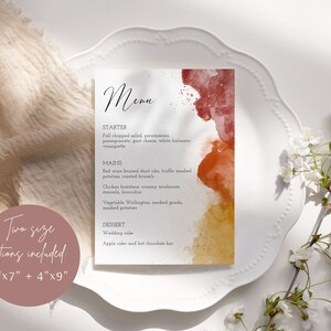 May include: A printable wedding menu card with a watercolor background in shades of red, orange, and yellow. The menu includes starter, mains, and dessert options. The text reads "Menu", "Starter", "Fall chopped salad, persimmons, pomegranate, goat cheese, white balsamic vinaigrette", "Mains", "Red wine braised short ribs, truffle mashed potatoes, roasted brussels", "Chicken forestiere, creamy mushroom marsala, broccolini", "Vegetable Wellington, smoked gouda, mashed potatoes", "Dessert", "Wedding cake", "Apple cider and hot chocolate bar".