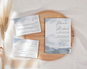 May include: Wedding invitation suite with a watercolor background in shades of blue. The invitation features the names "Adriana + Michael" and details about the wedding ceremony and reception. The RSVP card includes a reply section with options for "happily accepts", "number attending", and "regretfully declines".