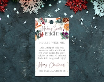 Può includere: Un'etichetta regalo bianca con un'illustrazione ad acquerello di vegetazione invernale, arance e bastoncini di cannella. Il testo recita "Making Spirits Bright" e include istruzioni per un mix di vino caldo. L'etichetta è decorata con glitter dorati e il testo "Merry Christmas!" in un carattere rosso festivo. La parte inferiore dell'etichetta recita "The Maclaughertys".