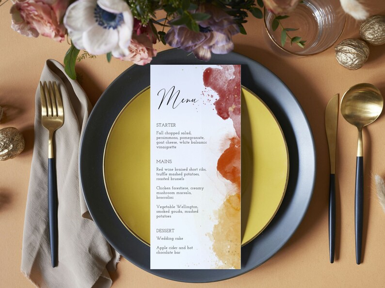 May include: A wedding menu card with a watercolor background in shades of red, orange, and yellow. The menu includes a starter, main courses, and dessert options. The text reads: "Menu", "Starter", "Fall chopped salad, persimmons, pomegranate, goat cheese, white balsamic vinaigrette", "Mains", "Red wine braised short ribs, truffle mashed potatoes, roasted brussels", "Chicken forestiere, creamy mushroom marsala, broccolini", "Vegetable Wellington, smoked gouda, mashed potatoes", "Dessert", "Wedding cake", "Apple cider and hot chocolate bar".