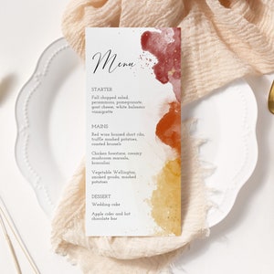 May include: A wedding menu with a watercolor background in shades of red, orange, and yellow. The menu lists the starter, mains, and dessert options. The text reads: "Menu", "Starter", "Fall chopped salad, persimmons, pomegranate, goat cheese, white balsamic vinaigrette", "Mains", "Red wine braised short ribs, truffle mashed potatoes, roasted brussel", "Chicken forestiere, creamy mushroom mariala, broccolini", "Vegetable Wellington, smoked gouda, mashed potatoes", "Dessert", "Wedding cake", "Apple cider and hot chocolate bar".