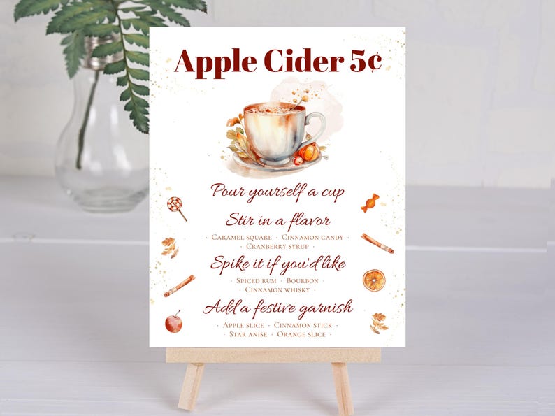 May include: A white sign with the text "Apple Cider 5&cent;" in red lettering. The sign has a watercolor illustration of a cup of apple cider with fall-themed garnishes. The sign also includes instructions for making apple cider with different flavors and garnishes.