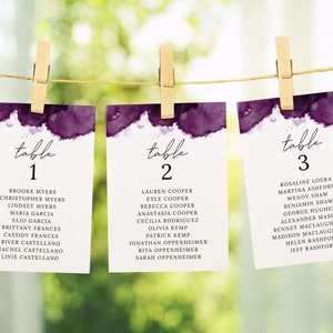 Peut inclure: Trois cartes de numéro de table avec des motifs aquarelle violet et blanc. Les cartes sont étiquetées "table 1", "table 2" et "table 3" avec une liste de noms sous chaque numéro.