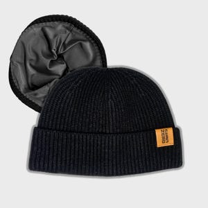 May include: Black knitted beanie with a brown leather patch that says "SUMF ZERO". The beanie has a fold-over brim and a soft, gray lining.