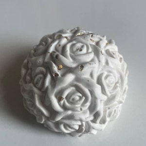 Op de afbeelding: Witte keramische bol met een textuur, die lijkt op een boeket rozen. De bol is versierd met gouden accenten.