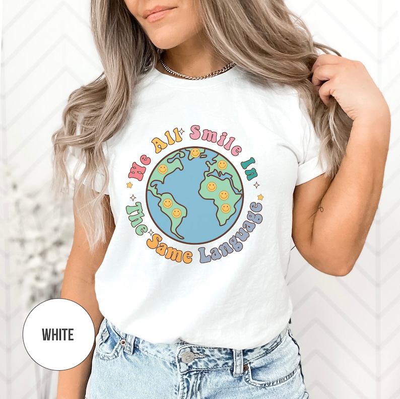 May include: White t-shirt with a colorful graphic of a globe with smiley faces and the text "We All Smile In The Same Language".