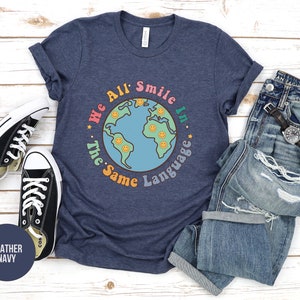May include: A heather navy blue t-shirt with a graphic of a blue globe with smiley faces and the text "We All Smile In The Same Language".