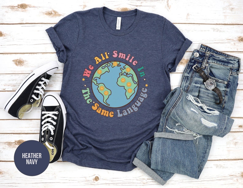 May include: A heather navy blue t-shirt with a graphic of a blue globe with smiley faces and the text "We All Smile In The Same Language".