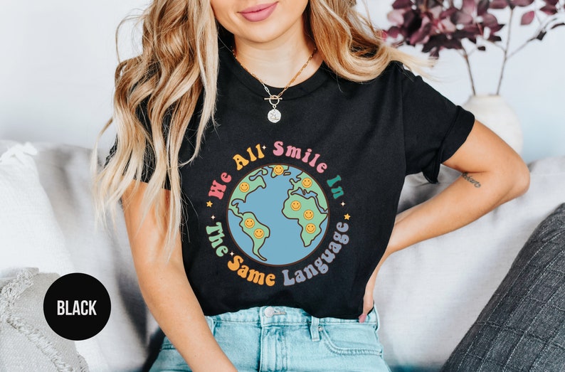 May include: Black t-shirt with a graphic of a blue and green earth with smiling faces and the text "We All Smile In The Same Language".