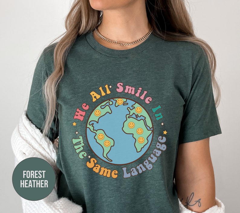 May include: A green t-shirt with a graphic of a blue and green earth with smiley faces. The text "We All Smile In The Same Language" is written around the earth in rainbow colors.