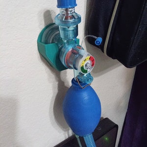May include: A blue and green medical breathing device with a blue bag attached to it. The device has a gauge with a red, yellow, and green color scale. The gauge reads 30, 40, and 50.