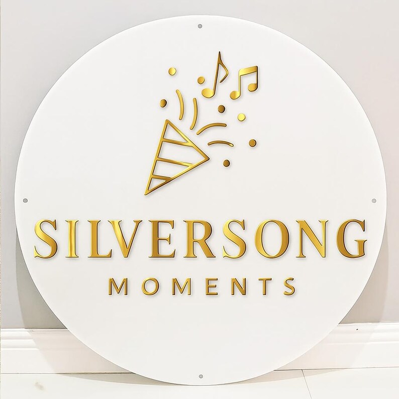 May include: A round white sign with gold lettering and accents. The text "SILVERSONG MOMENTS" is displayed in a bold, gold font. Above the text is a gold confetti popper and musical notes.