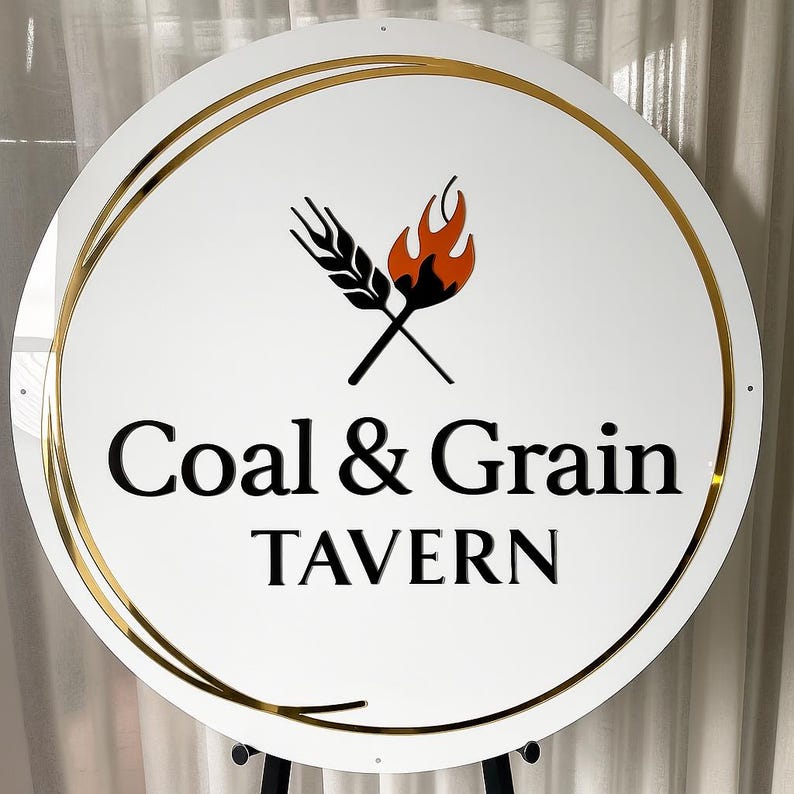 Może przedstawiać: Okrągły biały znak ze złotą obw&oacute;dką i czarnym napisem "Coal & Grain Tavern". Znak zawiera logo skrzyżowanych kłos&oacute;w pszenicy i płomienia w kolorze czarnym i pomarańczowym.