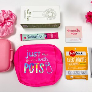 Puede incluir: Una colecci&oacute;n de accesorios y art&iacute;culos de salud rosas, que incluyen un ventilador peque&ntilde;o, una scrunchie, un estuche de viaje, una bolsa con el texto "just a girl with POTS", paquetes de electrolitos y toallitas desodorantes. Flores rosas en el fondo.