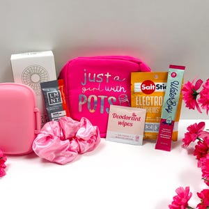 Puede incluir: Una colecci&oacute;n de art&iacute;culos rosas, que incluyen una fiambrera, una goma para el pelo y una bolsa de cosm&eacute;ticos con el texto "just a girl with POTS". Otros art&iacute;culos incluyen paquetes de electrolitos, toallitas desodorantes y un stick de hidrataci&oacute;n Waterboy.