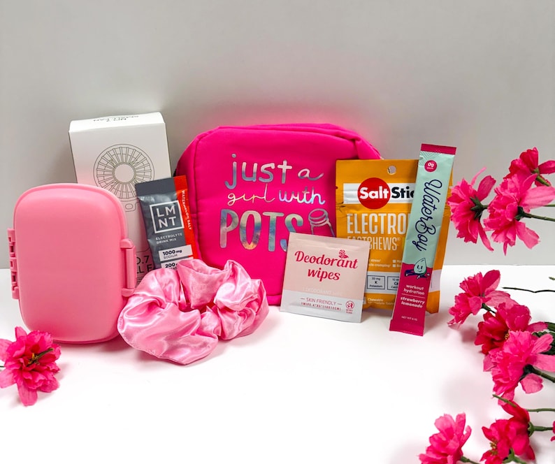 Puede incluir: Una colecci&oacute;n de art&iacute;culos rosas, que incluyen una fiambrera, una goma para el pelo y una bolsa de cosm&eacute;ticos con el texto "just a girl with POTS". Otros art&iacute;culos incluyen paquetes de electrolitos, toallitas desodorantes y un stick de hidrataci&oacute;n Waterboy.