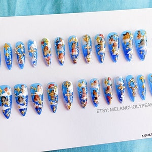 May include: A set of 20 blue and white press-on nails with gold accents and images of cherubs. The nails are arranged in two rows on a white background. The text "ETSY: MELANCHOLY PEARLS" is printed on the bottom right corner of the image. The text "MELANCHOLY PEARLS" is printed on the bottom right corner of the image.