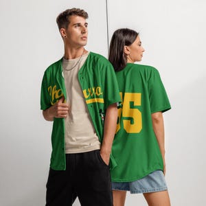 May include: Green baseball jersey with yellow lettering and the number 55 on the back. The jersey has a button-up front and short sleeves. The front of the jersey has the text "Tha Uva" in yellow. The jersey is worn by two people.