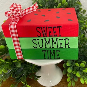 以下が含まれることがあります： スイカのようにペイントされた3つの木製ブロックのスタック。 上部のブロックは赤で黒い種があり、下部の2つのブロックには黒い文字で「Sweet Summer Time」と書かれています。
