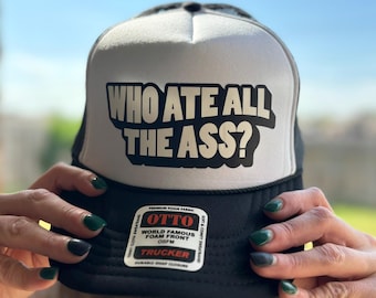 Könnte beinhalten: Schwarz-weiße Trucker-Cap mit dem Text "WHO ATE ALL THE ASS?" in fetten, schwarzen Buchstaben. Die Kappe hat eine weiße Schaumstofffront und eine schwarze Mesh-Rückseite. Die Kappe hat auch ein Etikett mit der Aufschrift "OTTO" und "TRUCKER".