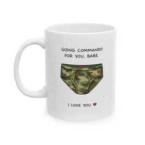 Könnte beinhalten: Weißer Keramikbecher mit Henkel. Der Becher zeigt den Text "GOING COMMANDO FOR YOU, BABE." über einer Cartoon-Darstellung von Tarnungsunterwäsche. Darunter steht der Text "I LOVE YOU." mit einem Herzsymbol.